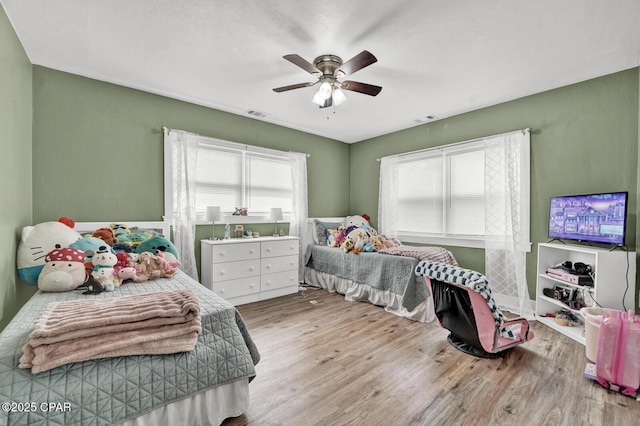 bedroom with a ceiling fan, visible vents, and wood finished floors