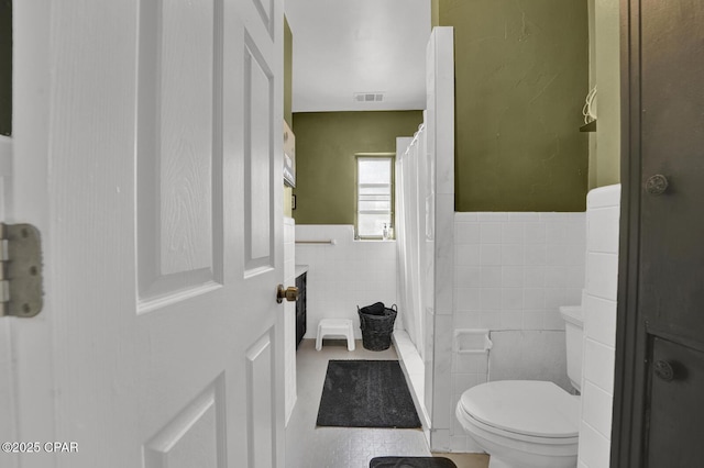 full bathroom featuring a wainscoted wall, a shower with shower curtain, toilet, tile walls, and tile patterned flooring