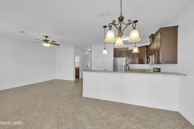 kitchen featuring visible vents, ceiling fan with notable chandelier, a peninsula, a breakfast bar, and stainless steel appliances