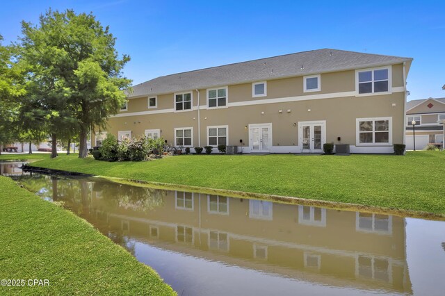 back of property featuring french doors, a water view, a lawn, and stucco siding