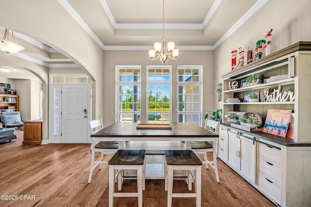 dining space featuring an inviting chandelier, arched walkways, a tray ceiling, and light wood-type flooring