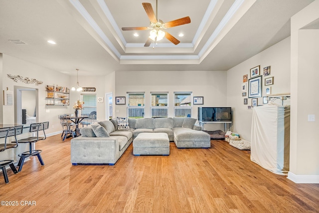 living room featuring light wood-style floors, recessed lighting, crown molding, and a tray ceiling