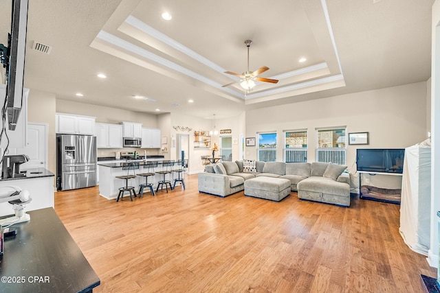 living area with a ceiling fan, crown molding, a raised ceiling, light wood finished floors, and recessed lighting