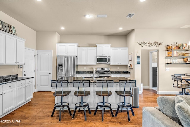 kitchen with light wood-style flooring, white cabinetry, a kitchen breakfast bar, and stainless steel appliances