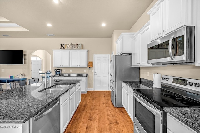kitchen with a sink, arched walkways, white cabinets, and stainless steel appliances
