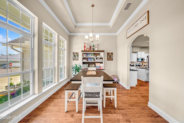 dining area with a notable chandelier, plenty of natural light, light wood-style flooring, and a raised ceiling