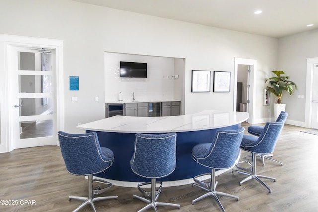kitchen featuring light stone counters, wine cooler, wood finished floors, and a kitchen breakfast bar