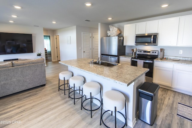 kitchen featuring appliances with stainless steel finishes, a breakfast bar, a sink, light wood-style floors, and white cabinetry
