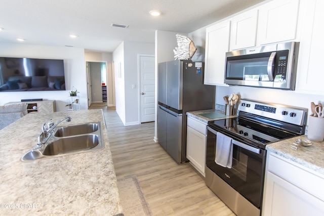 kitchen featuring light countertops, white cabinetry, a sink, light wood-style flooring, and appliances with stainless steel finishes