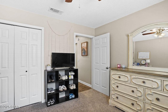 bedroom with a closet, a textured ceiling, visible vents, dark colored carpet, and a ceiling fan