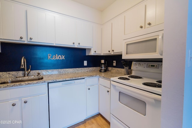 kitchen with light stone counters, a sink, white cabinets, and white appliances