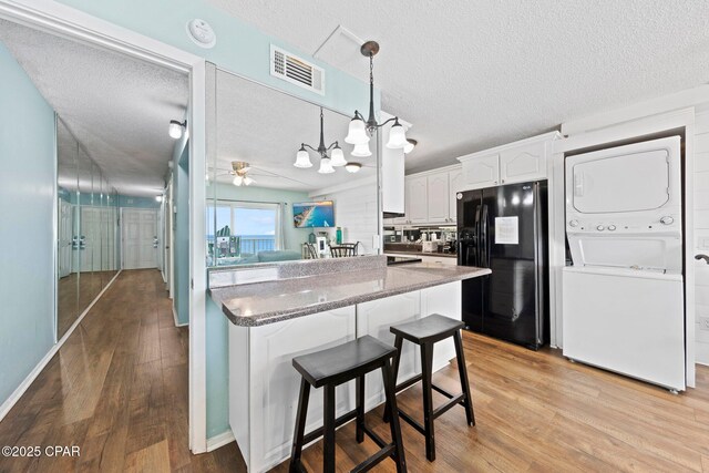 8743 Thomas Dr Unit 809, Panama City Beach, FL 32408 - kitchen with black fridge, stacked washer / dryer, a textured ceiling, white cabinets, and a breakfast bar