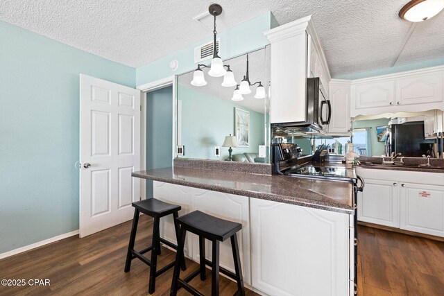 8743 Thomas Dr Unit 809, Panama City Beach, FL 32408 - kitchen with white cabinetry, a textured ceiling, a breakfast bar, dark wood finished floors, and black appliances