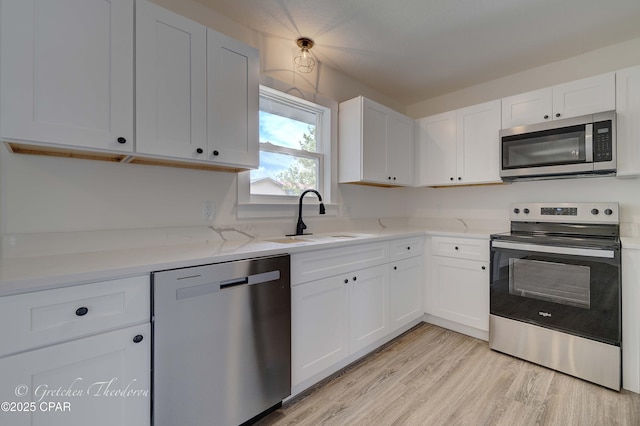 kitchen with appliances with stainless steel finishes, white cabinetry, a sink, light stone counters, and light wood-style flooring