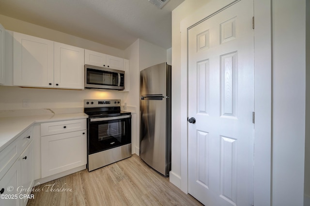 kitchen with visible vents, appliances with stainless steel finishes, light countertops, white cabinets, and light wood-style floors