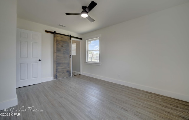unfurnished bedroom featuring ceiling fan, a barn door, baseboards, wood finished floors, and visible vents