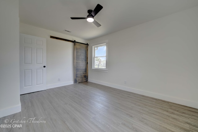 unfurnished bedroom featuring a barn door, a ceiling fan, baseboards, wood finished floors, and visible vents