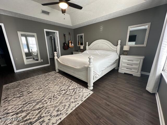 bedroom with baseboards, a tray ceiling, dark wood-type flooring, and visible vents