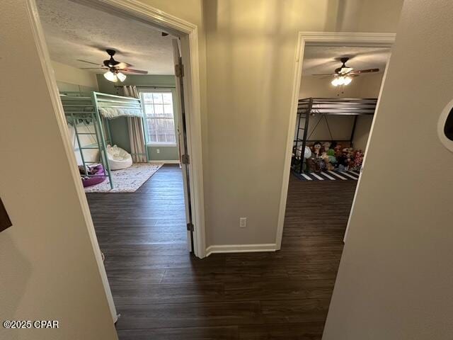 corridor with a textured ceiling, baseboards, and wood finished floors