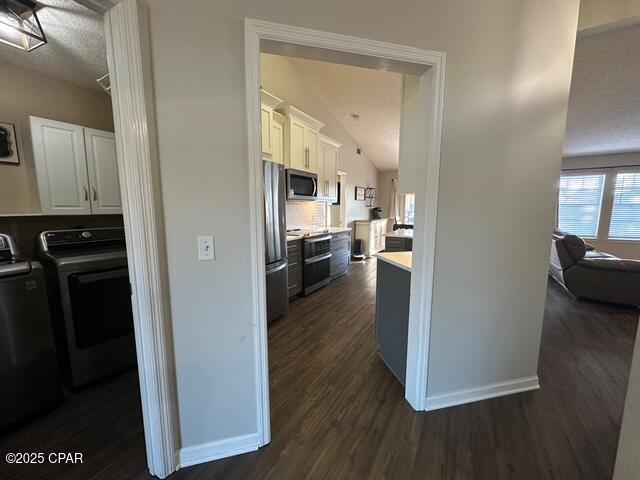 kitchen featuring baseboards, dark wood-type flooring, white cabinets, vaulted ceiling, and stainless steel appliances