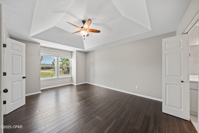 spare room with dark wood-type flooring, a ceiling fan, a raised ceiling, and baseboards