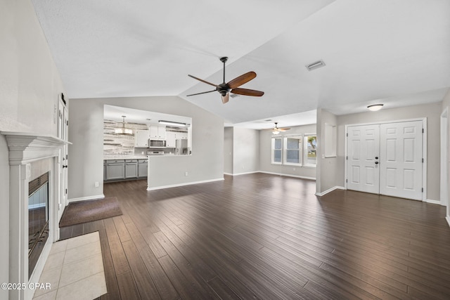 unfurnished living room featuring dark wood-style flooring, ceiling fan, lofted ceiling, a tile fireplace, and visible vents