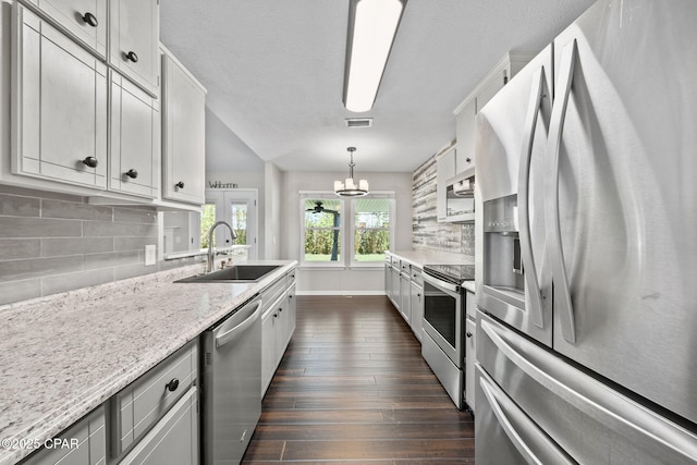 kitchen with decorative backsplash, a sink, a chandelier, stainless steel appliances, and dark wood-type flooring