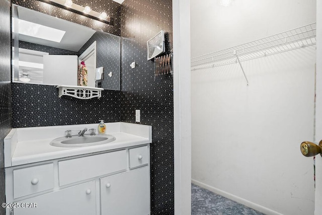 bathroom featuring vanity, baseboards, a skylight, and wallpapered walls