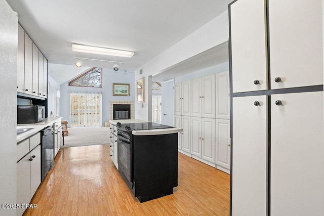 kitchen featuring dishwasher, vaulted ceiling, light wood-style flooring, and a fireplace