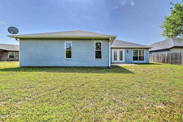 rear view of house with french doors, fence, stucco siding, and a yard