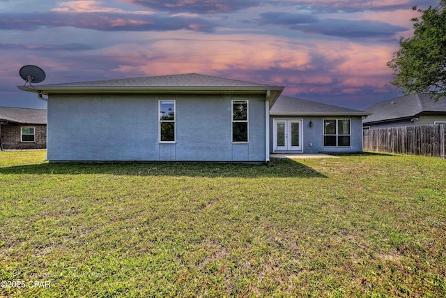 back of property with a lawn, stucco siding, fence, and french doors