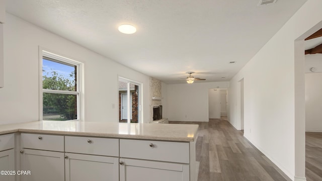 325 Bell Cir, Lynn Haven, FL 32444 - kitchen featuring a peninsula, light wood-style flooring, a ceiling fan, a large fireplace, and white cabinets