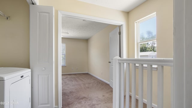 hallway with washer / clothes dryer, baseboards, and light carpet