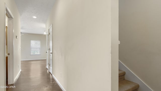 hall with finished concrete floors, a textured ceiling, baseboards, and stairway