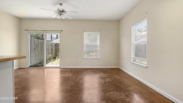 spare room with plenty of natural light, a ceiling fan, and concrete flooring