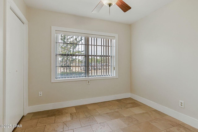 unfurnished room with a healthy amount of sunlight, baseboards, ceiling fan, and stone finish floor
