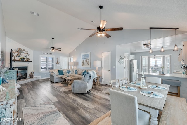 dining space featuring a ceiling fan, wood finished floors, high vaulted ceiling, a glass covered fireplace, and baseboards