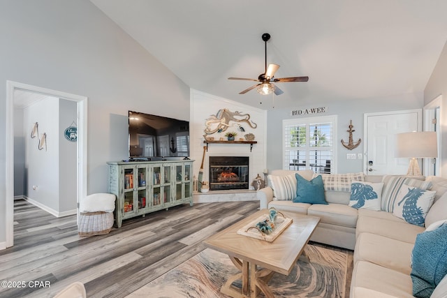 living room with a ceiling fan, lofted ceiling, wood finished floors, a large fireplace, and baseboards