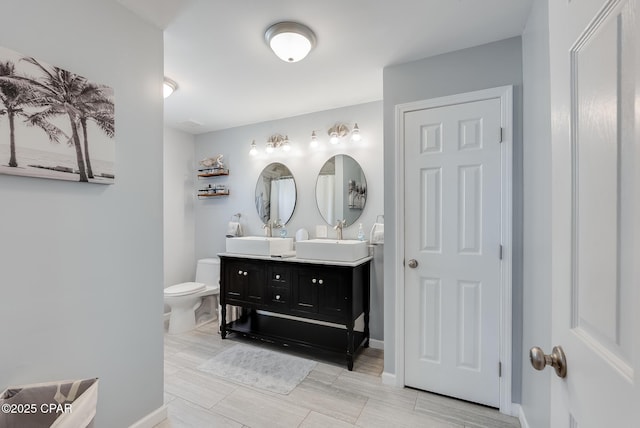 full bath with toilet, double vanity, and baseboards
