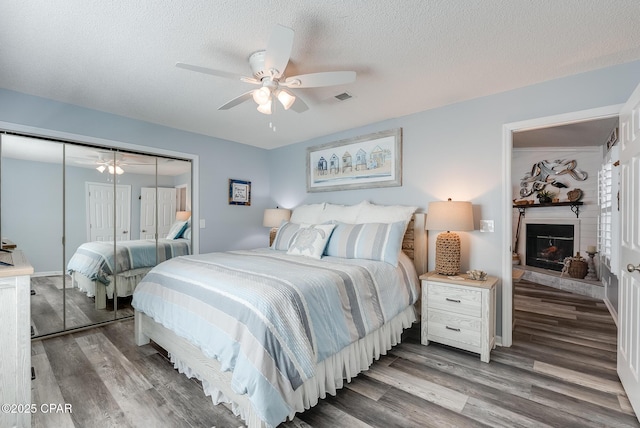 bedroom featuring wood finished floors, a closet, a fireplace with raised hearth, a ceiling fan, and a textured ceiling