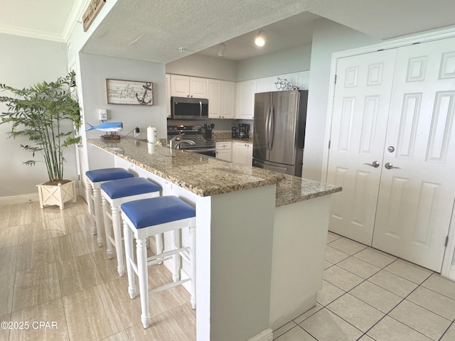 kitchen featuring light stone countertops, light tile patterned floors, white cabinets, a peninsula, and stainless steel appliances