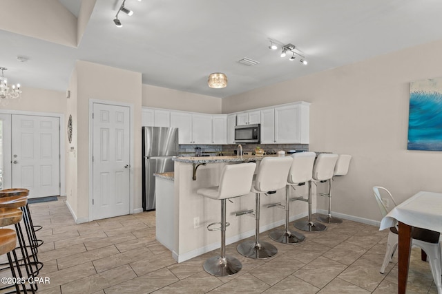 kitchen with a peninsula, a breakfast bar area, white cabinets, rail lighting, and appliances with stainless steel finishes