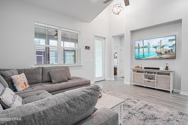 living area with baseboards, ceiling fan, wood finished floors, and high vaulted ceiling