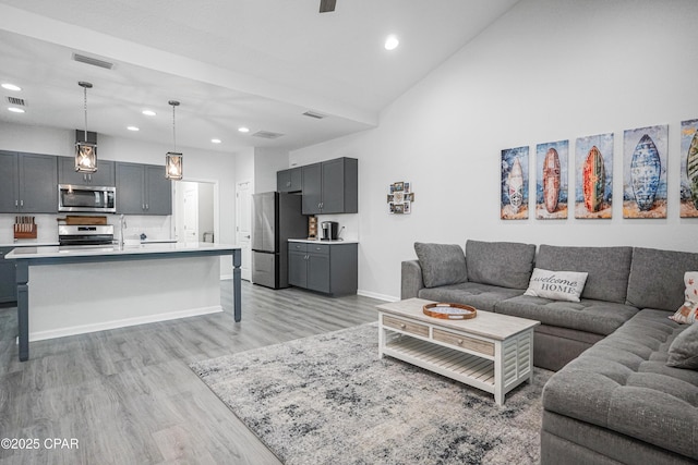 living room featuring visible vents, baseboards, high vaulted ceiling, light wood finished floors, and recessed lighting