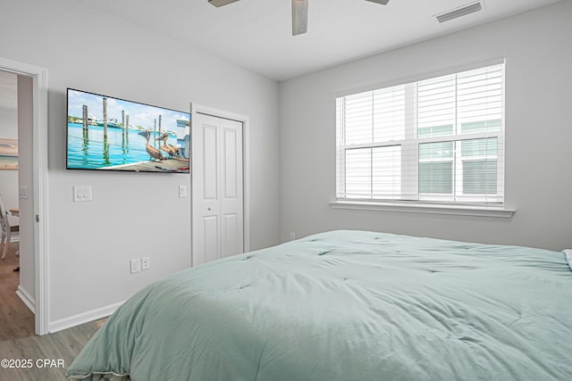 bedroom featuring ceiling fan, visible vents, wood finished floors, baseboards, and a closet