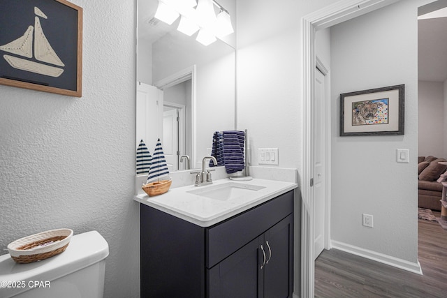 half bath featuring a textured wall, vanity, toilet, baseboards, and wood finished floors
