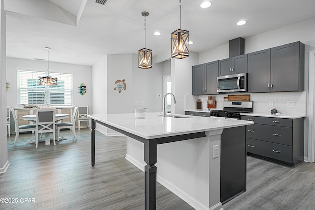 kitchen with an inviting chandelier, a sink, light wood finished floors, light countertops, and stainless steel appliances