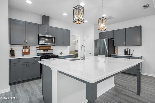 kitchen with appliances with stainless steel finishes, a sink, baseboards, wood finished floors, and visible vents