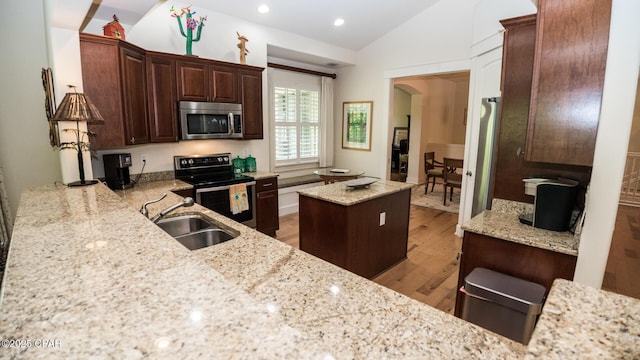 kitchen with light stone countertops, light wood-type flooring, a sink, lofted ceiling, and stainless steel appliances