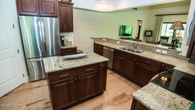 kitchen featuring dark brown cabinetry, light stone countertops, light wood-type flooring, a sink, and stainless steel appliances
